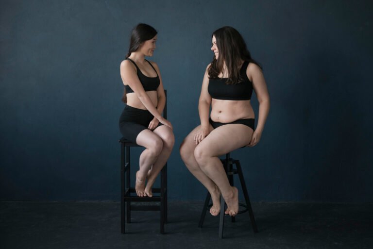 Duas mulheres de biotipos diferentes sentadas, ilustrando a comparação de corpos e a possível presença de Lipedema em pernas e braços, mesmo em diferentes pesos.