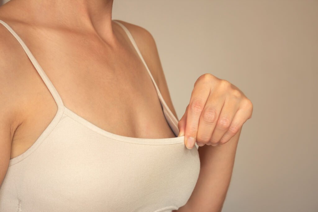 Jovem com roupa íntima bege retira o top e observa suas mamas pequenas – mamoplastia de aumento